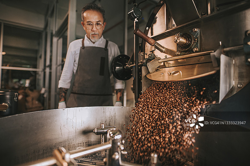 亚洲资深手工艺人观察新鲜烘焙的咖啡豆从烘焙机移到冷却缸与运动模糊图片素材
