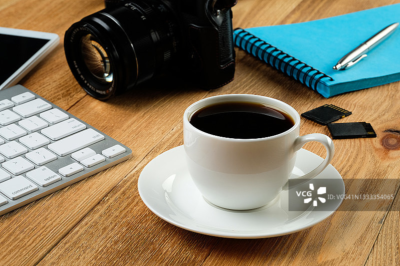 一个手机，一个笔记本电脑键盘，一支笔和记事本，一个咖啡杯，闪存驱动器和木桌上的相机。摄影师工作场所的物品。概念爱好，专业摄影服务。图片素材