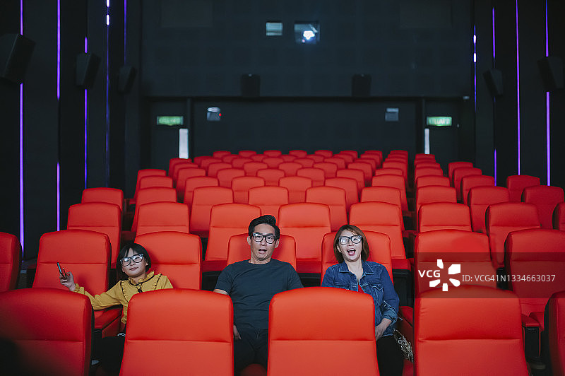 亚洲华人家庭带着一个孩子在电影院看3D电影，戴着3D眼镜图片素材