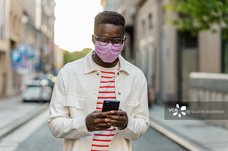 非裔美国年轻人戴着防护口罩，一边走路一边用手机图片素材