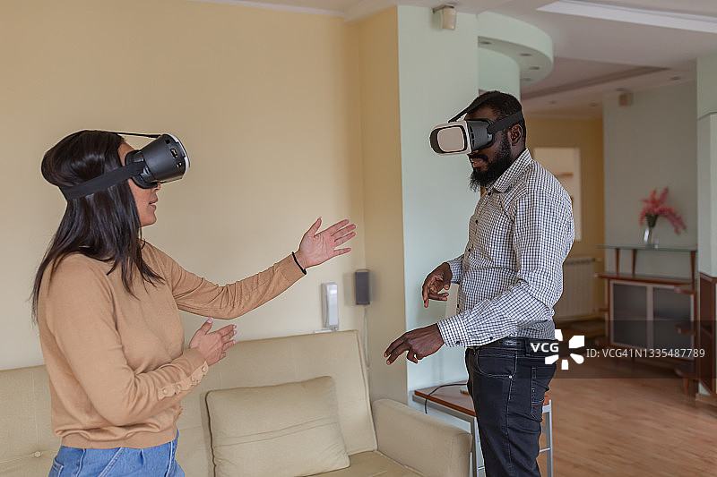 一位快乐的年轻女子正和男友在客厅用虚拟现实系统玩电脑游戏。图片素材