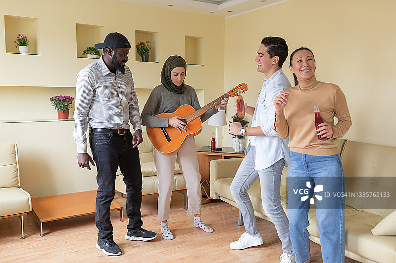 一名年轻的穆斯林女子在现代公寓里弹吉他，她的朋友们在跳舞。图片素材