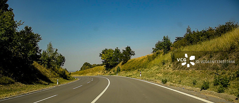 柏油路在一个阳光明媚的夏日里绿油油的田野上，蓝色的云天背景下。图片素材
