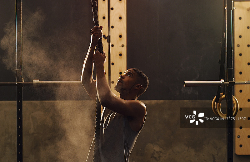 一个肌肉发达的年轻人在健身房爬绳子图片素材