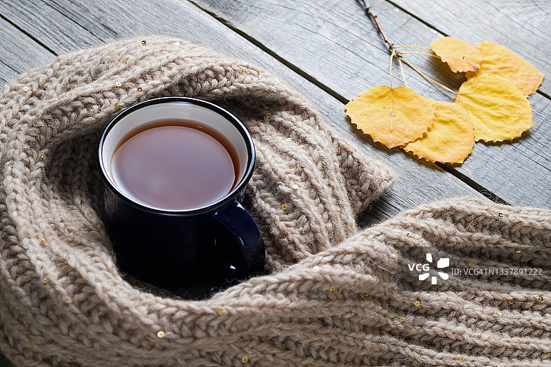 热咖啡或茶在一个杯子，明亮的秋天黄色的树叶，一条温暖舒适的针织羊毛围巾，背景是一个古老的木制背景或桌子。季节性的娱乐、放松和心灵的宁静。文本空间的拷贝。图片素材