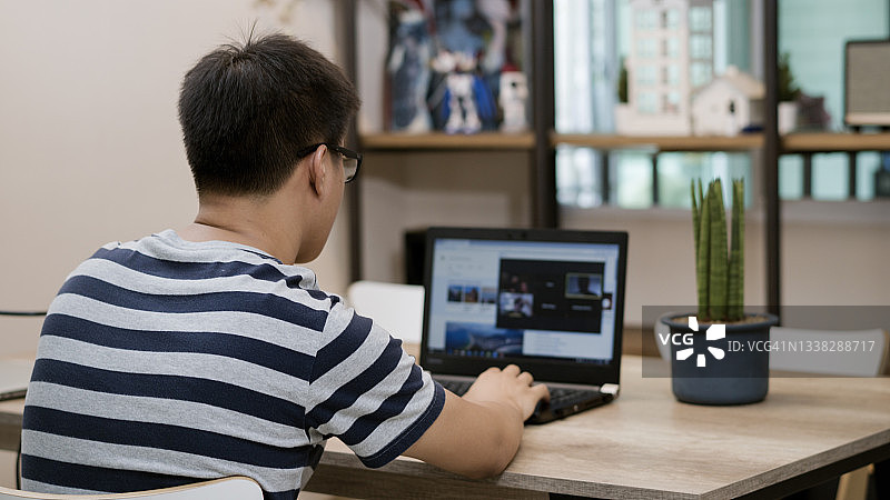 一名年轻人正在家中办公室的电脑屏幕上参加团队电话会议。图片素材