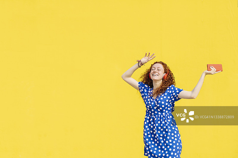 一个欢快的女人在黄色的墙前跳舞图片素材