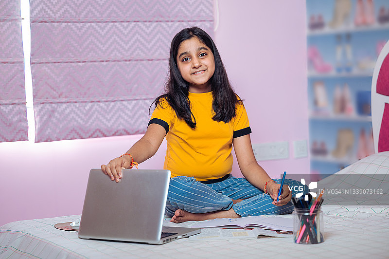 小女孩在床上用笔记本电脑和智能手机学习。图片素材