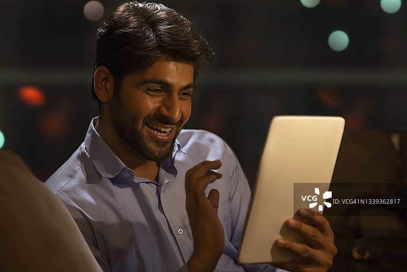一个快乐的年轻人在晚上工作时使用电子平板电脑图片素材