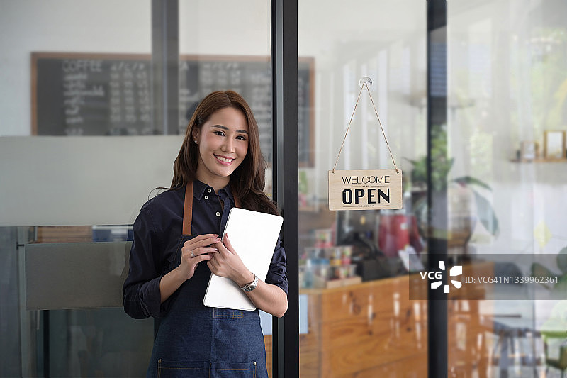 微笑的女服务员手持电子平板电脑，站在现代咖啡馆。图片素材