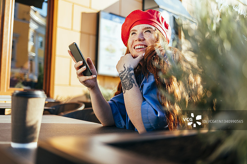 拿着智能手机的快乐女人在路边咖啡馆沉思图片素材