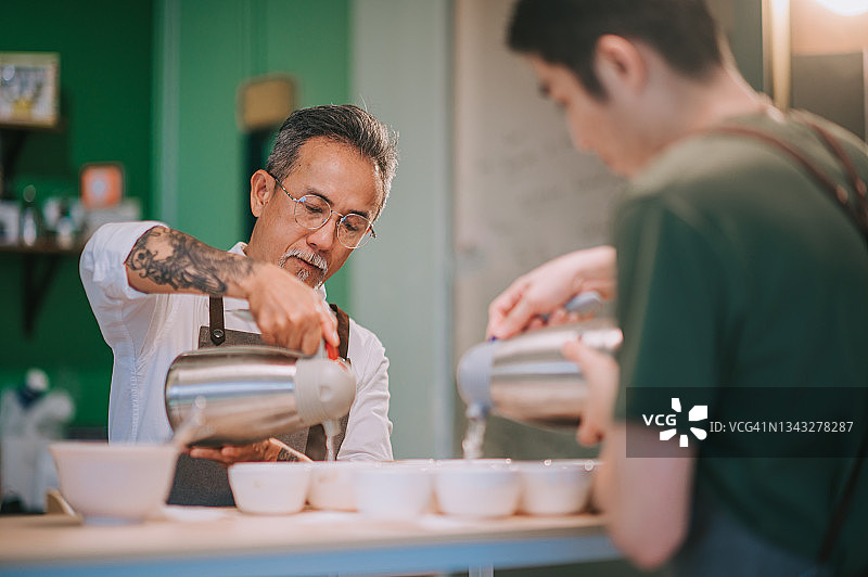 2 .专业亚洲华人咖啡师将热水倒入陶瓷咖啡杯中，为咖啡的拔火罐准备咖啡品质测试图片素材