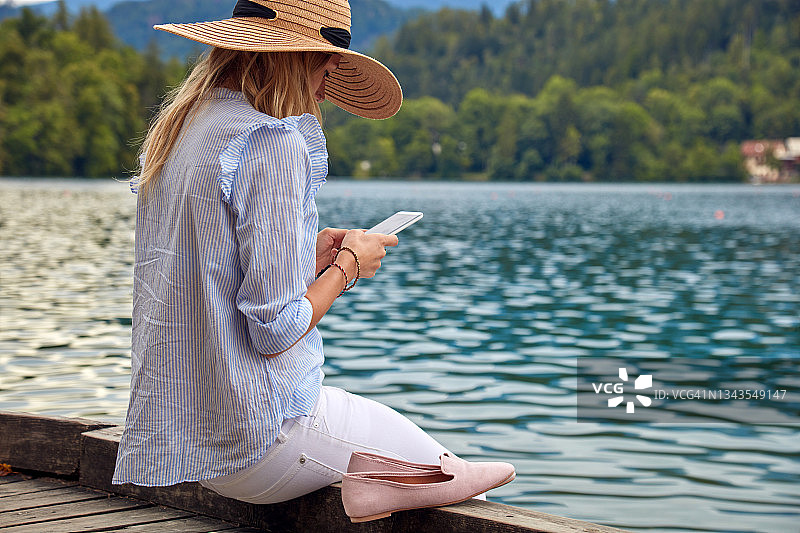 年轻的成年女游客享受在湖上用现代智能手机拍照。图片素材
