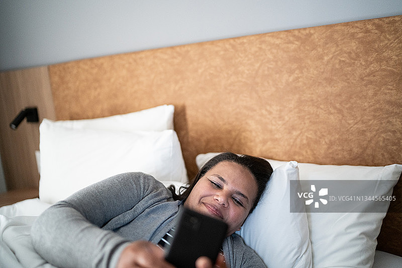 快乐的成熟女人在床上玩手机图片素材