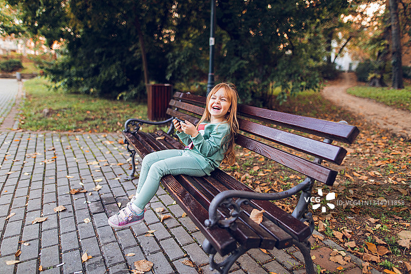 微笑的小女孩在户外使用智能手机图片素材