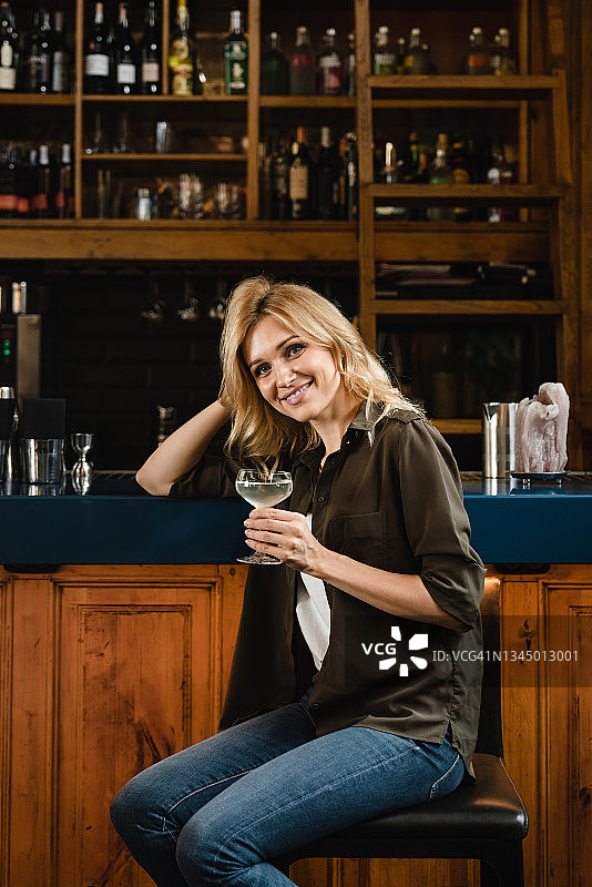 一个成功的年轻白人女学生的垂直肖像，在酒吧柜台餐厅放松的时候，喝着气泡酒鸡尾酒庆祝活动图片素材