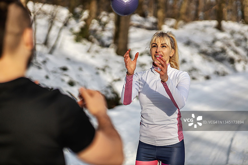运动情侣站在雪地里，在冬天用健身球做热身运动。冬季健身、人际关系、亲密关系图片素材