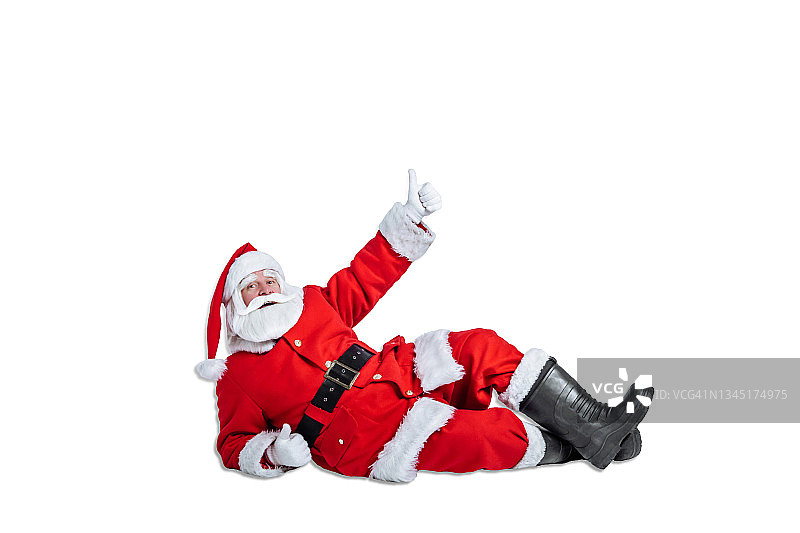 圣诞老人躺在地板上，在白色的背景上做竖起大拇指的手势。圣诞节广告和销售概念图片素材