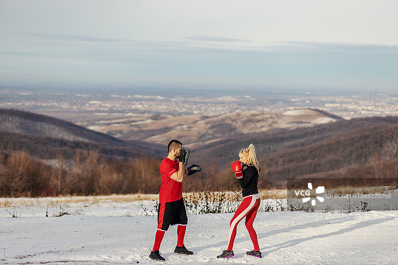 女运动员在雪天与她的教练在自然界拳击手套。拳击，冬季健身，户外健身图片素材