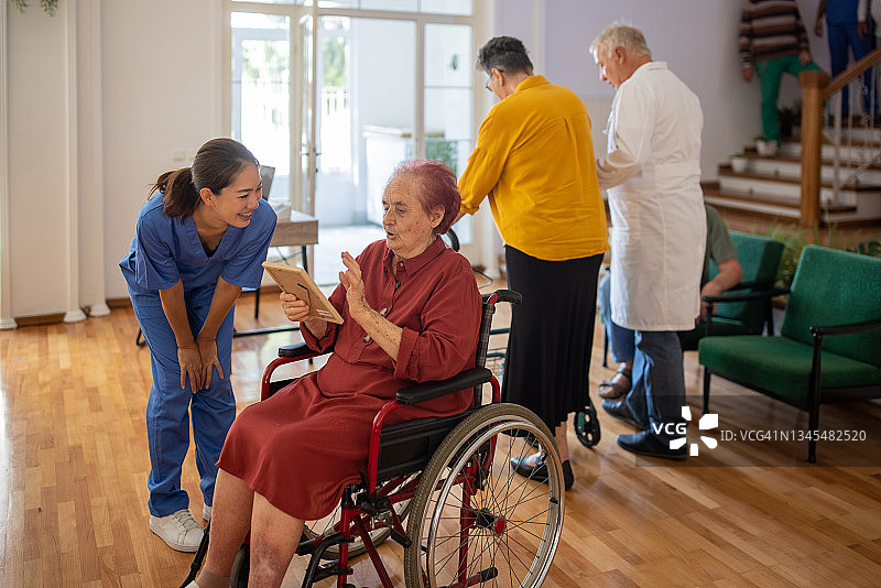 坐在轮椅上的老妇人看着她的照片，和护士谈论她在疗养院的过去图片素材