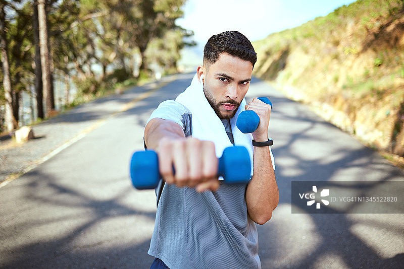 一个运动的年轻人的肖像做哑铃出拳，同时在户外锻炼图片素材