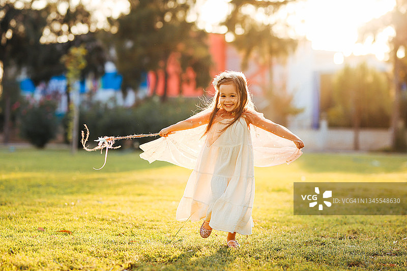 小女孩穿着仙女的衣服，拿着魔杖，在绿草地上昂首阔步图片素材