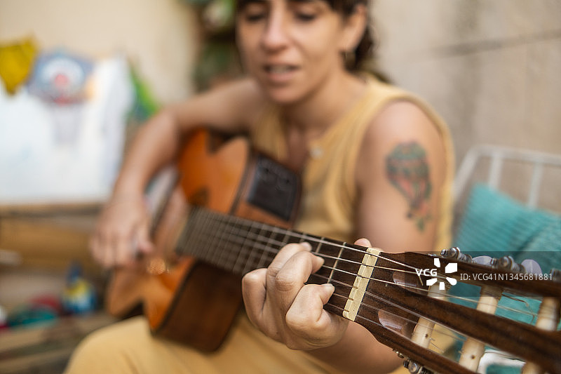 年轻的拉丁妇女喜欢在家里弹吉他。选择性聚焦于左手图片素材