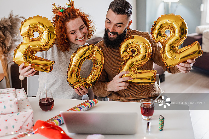 一对年轻夫妇手持数字“2022”形状的气球，在网上庆祝新年图片素材