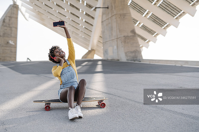 一个非洲女人坐在户外滑板上用手机和耳机听音乐。图片素材