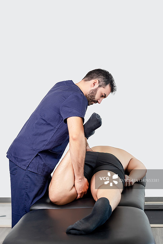 留胡子的理疗师正在帮助躺在担架上的病人弯曲膝盖。图片素材