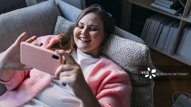 一个胖女人躺在沙发上用手机和朋友视频通话图片素材