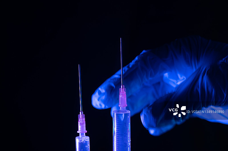 一个戴着防护手套的人将拿着一支注射器准备注射疫苗。Covid-19疫苗的概念。图片素材