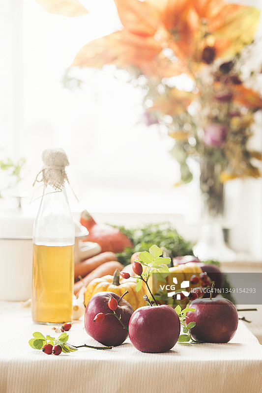 白色的餐桌上摆放着红苹果和五颜六色的蔬菜，窗台上放着醋瓶和秋天的花束图片素材