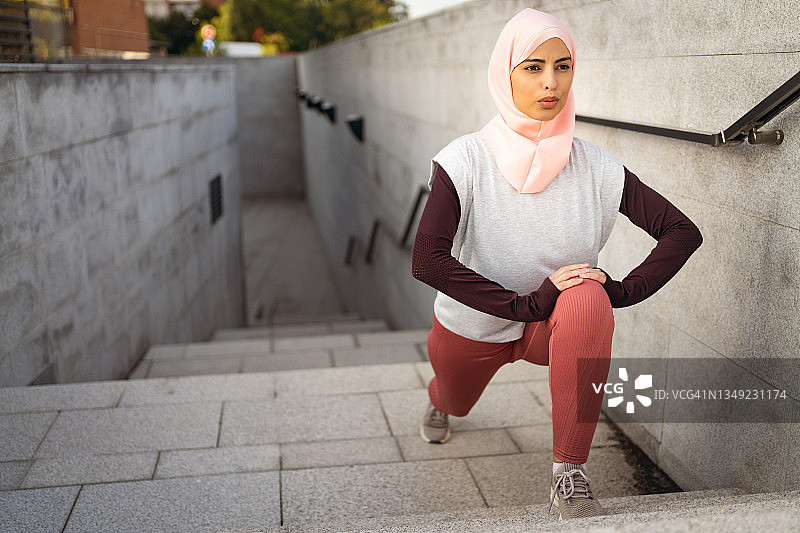 专注的穆斯林女运动员在楼梯上伸展双腿图片素材