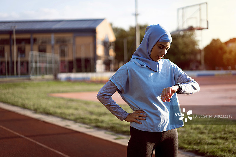 现代穆斯林女运动员正在用健身追踪器检查自己的脉搏图片素材
