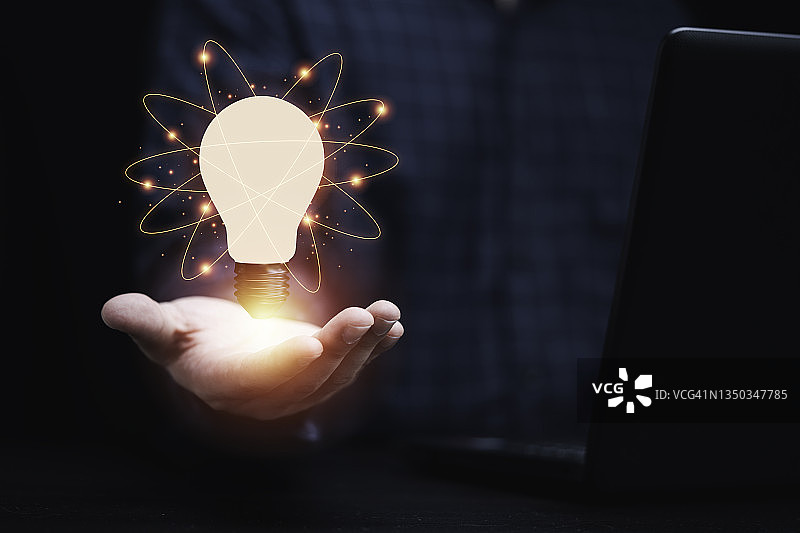 商人拿着发光的灯泡，用连接线，创造性的思维和创新的理念。图片素材