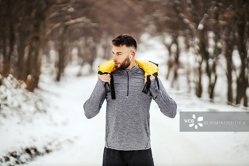 在下雪的冬天，健美运动员站在树林里，举着杠铃。健身,冬季健身图片素材