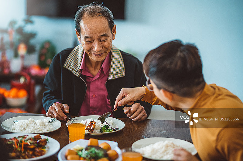 中国农历新年期间，一名亚洲男子在家里吃团圆饭时给他的父亲分享食物图片素材