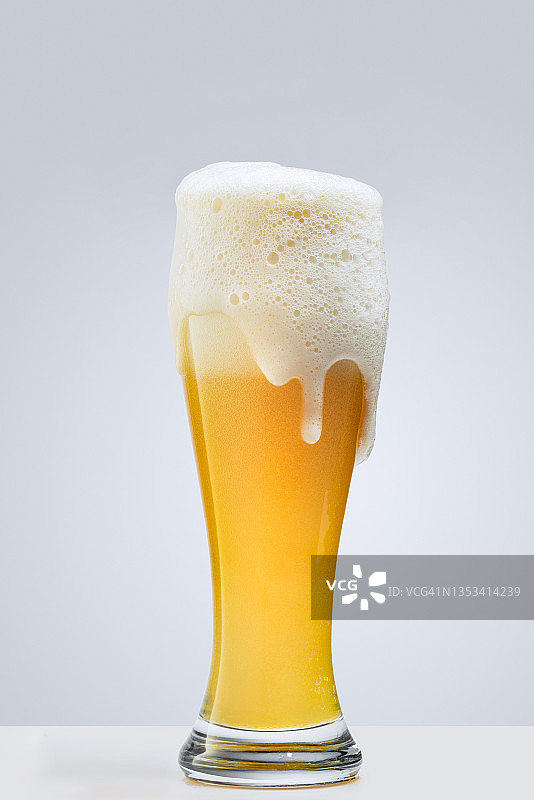 在灰色的背景下，一杯大杯的泡沫啤酒。酒精饮料的概念图片素材