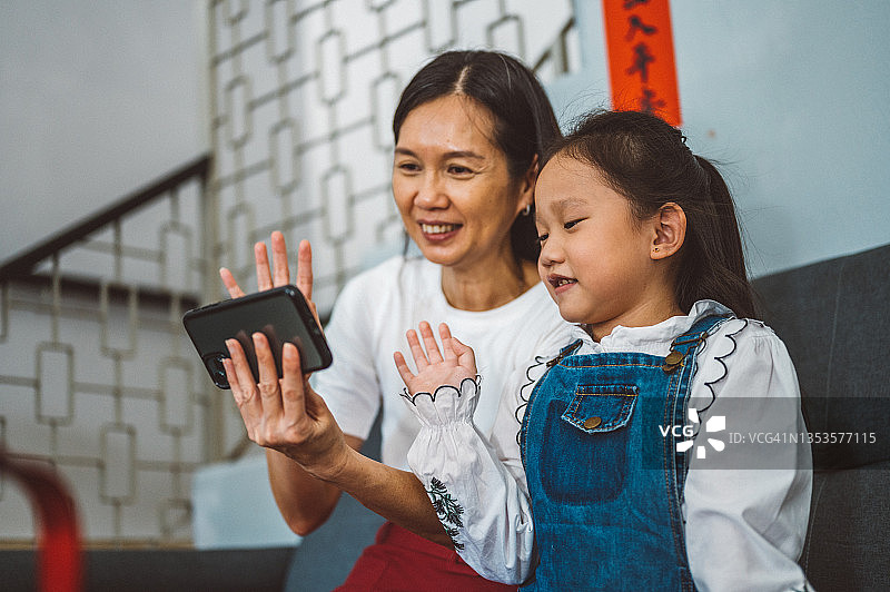 一个亚洲妈妈和一个小女孩在中国新年期间用智能手机视频通话图片素材