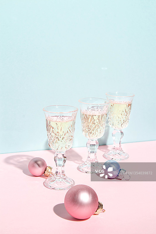 香槟酒杯，蓝色和粉红色柔和的背景与圣诞球。简约的艺术成分。圣诞节和新年节日派对的概念。图片素材