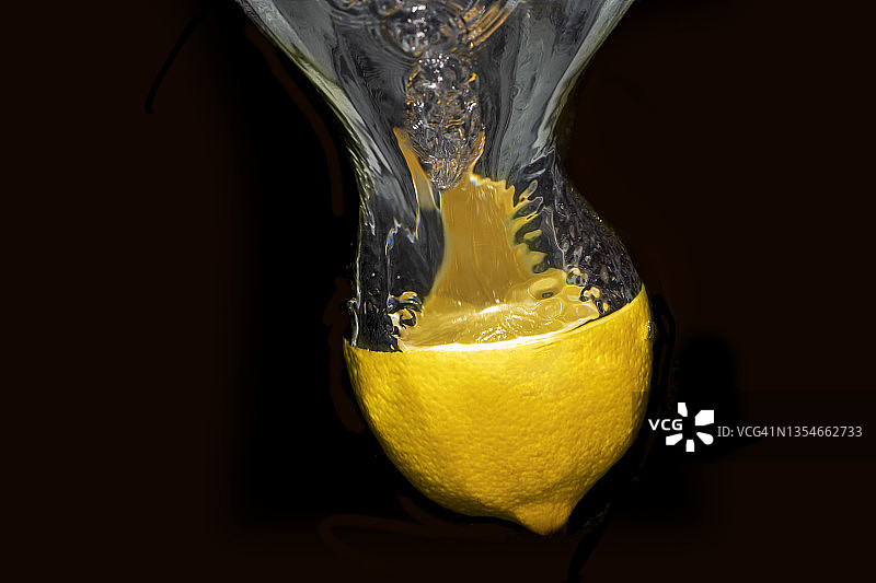 把半个柠檬扔进水里。水的气泡来自柠檬。这张照片的背景是黑色的图片素材