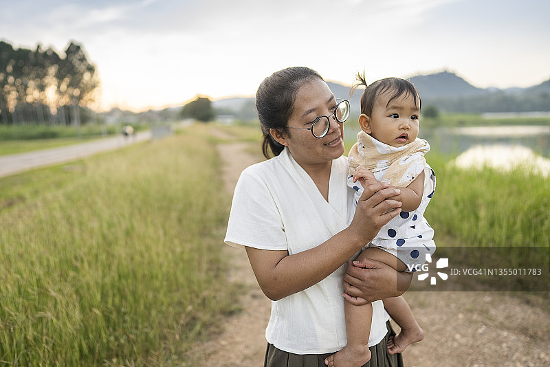 亚洲母亲穿着休闲的衣服，拥抱女儿休闲野餐，户外公园和家庭正常的生活方式图片素材