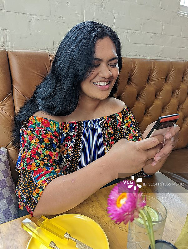 一位年轻女子在餐馆里用手机微笑图片素材