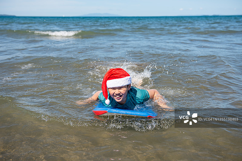 戴着圣诞帽的少年正在海滩上冲浪，享受着他的夏季圣诞节图片素材