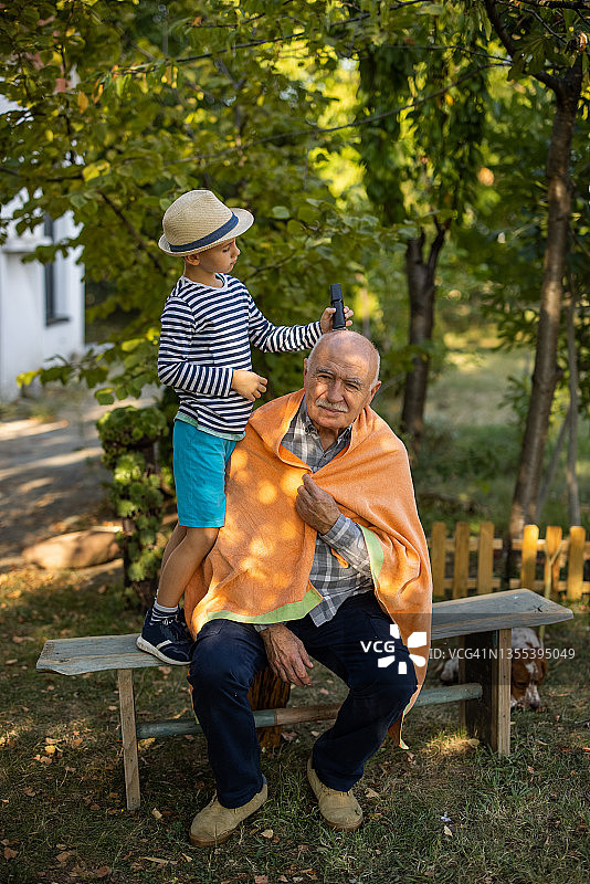 孙子在后院用电动剃刀给爷爷理发图片素材