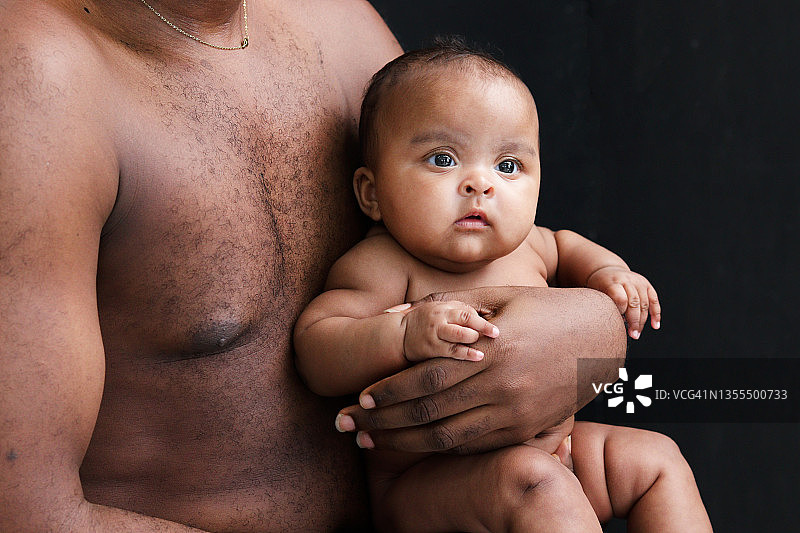 小亚洲非洲新生儿女孩在她爸爸的怀抱黑色的背景，肖像甜美可爱的婴儿在父亲的怀里，父母抱着婴儿。图片素材