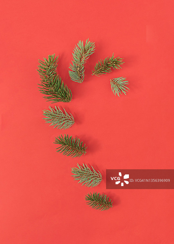 糖果手杖形状与常青圣诞树的树枝在大胆的红色背景。最小的新年概念。创造性的节日的想法。平的。图片素材