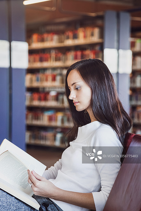 一个年轻的女人在图书馆看书。图片素材