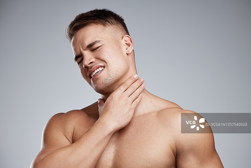 工作室拍摄了一个肌肉发达的年轻人在灰色背景下经历脖子疼痛图片素材